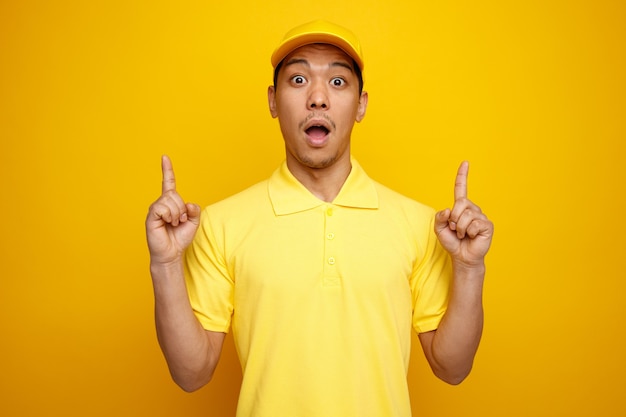 Impressed young delivery man wearing cap and uniform pointing up 