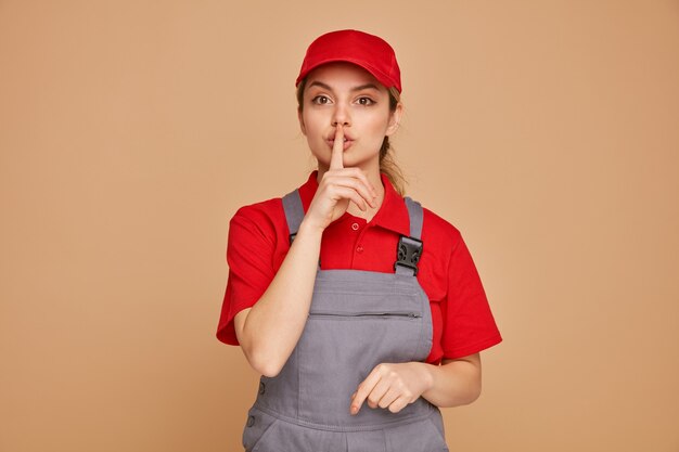 Impressionato giovane operaio edile femminile che indossa l'uniforme e berretto facendo gesto di silenzio