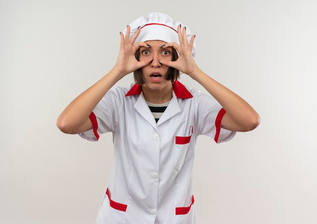 Impressed young female cook in chef uniform showing control sign isolated on white 