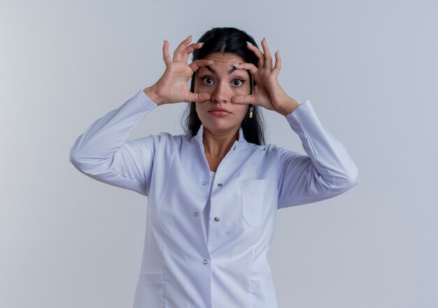 Impressed young female doctor wearing medical robe looking making big eyes isolated