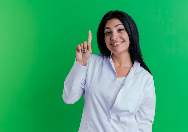 Впечатленная молодая женщина-врач в медицинском халате, улыбаясь и поднимая палец