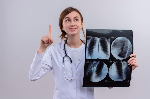 Impressed young female doctor wearing medical robe and stethoscope and holding x-ray shot raising finger 