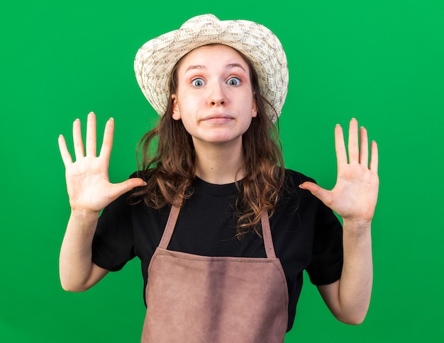 緑​の​壁​に​隔離された​手​を​上げる​ガーデニング​の​帽子​を​かぶって​感動​の​若い​女性​の​庭師