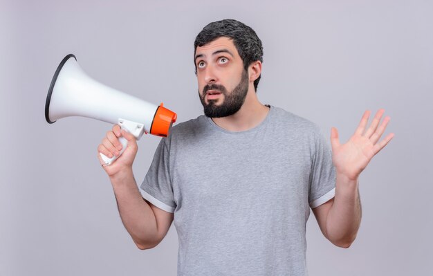 Impressed young handsome caucasian man holding speaker looking up and raising hand isolated on white 