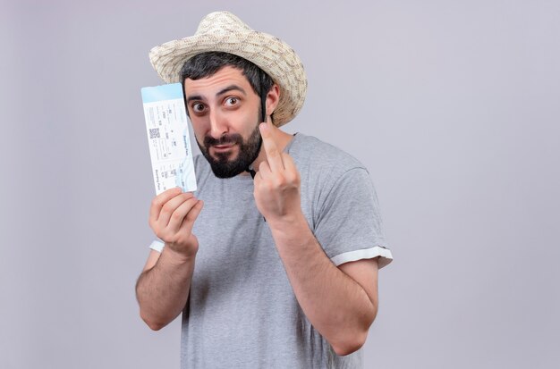 Впечатленный молодой красивый кавказский путешественник в шляпе, держащий билет на самолет и делающий жест средним пальцем, изолированный на белом с копией пространства