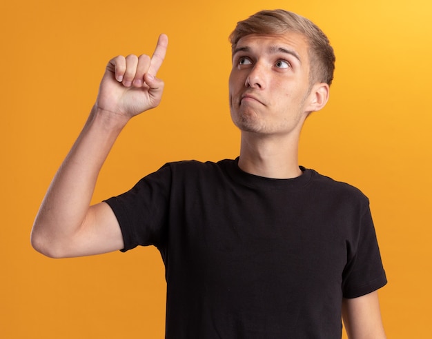 Free photo impressed young handsome guy wearing black shirt points at up isolated on yellow wall