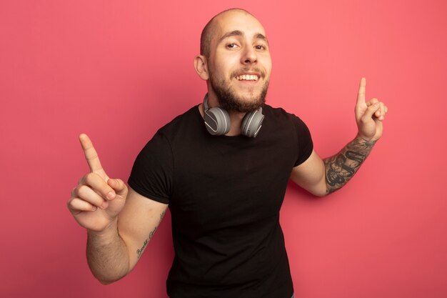 Free photo impressed young handsome guy wearing headphones on neck points at up