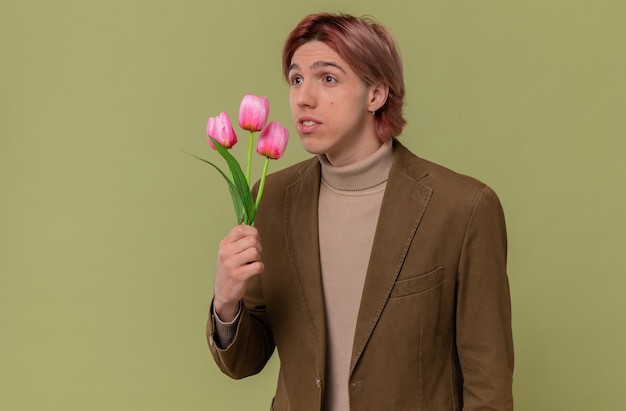 Impressed young handsome man holding flowers and looking at side