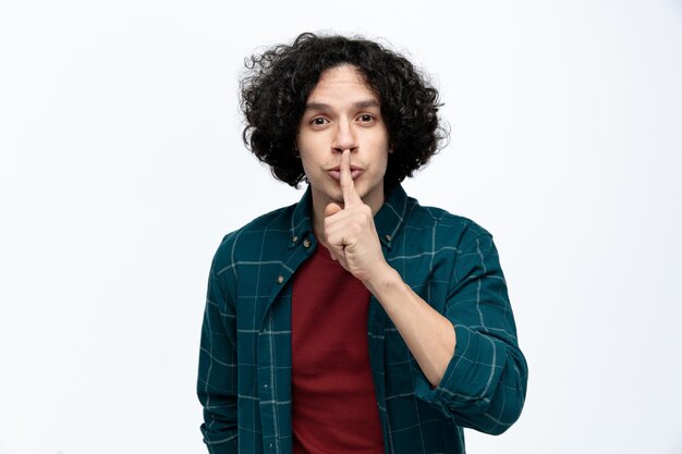 Impressed young handsome man looking at camera doing shh gesture isolated on white background