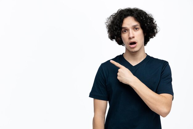 Impressed young handsome man looking at camera pointing to side isolated on white background with copy space