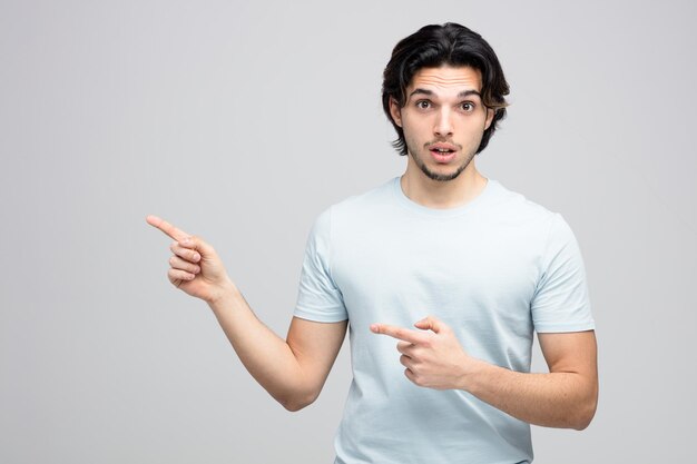 impressed young handsome man looking at camera pointing to side isolated on white background