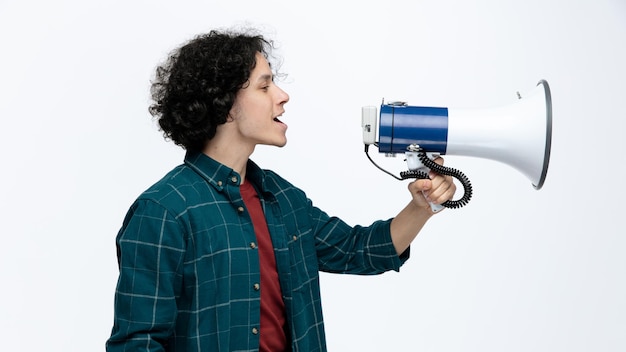 Free photo impressed young handsome man standing in profile view looking at side talking by loudspeaker isolated on white background