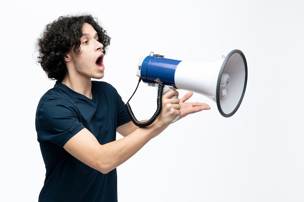 Free photo impressed young handsome man standing in profile view talking into speaker looking at side showing empty hand isolated on white background