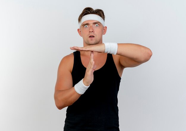 Free photo impressed young handsome sporty man wearing headband and wristbands doing timeout gesture isolated on white