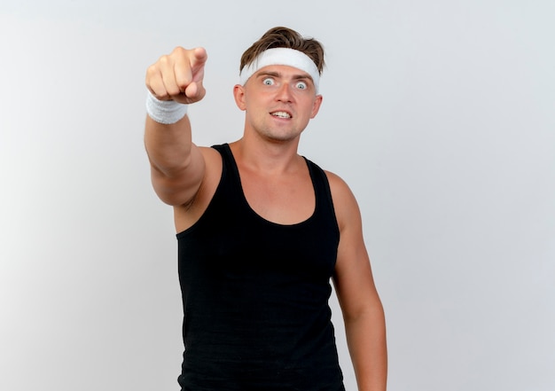 Impressed young handsome sporty man wearing headband and wristbands pointing at front isolated on white