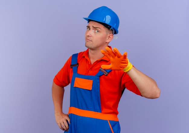Впечатлен молодой мужчина-строитель в униформе и защитном шлеме в перчатках, протягивая руку