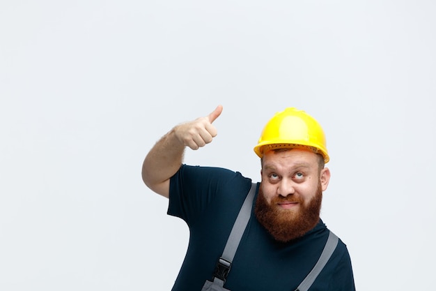 안전 헬멧과 유니폼을 입고 복사 공간이 있는 흰색 배경에 고립된 찾고 가리키는 젊은 남성 건설 노동자
