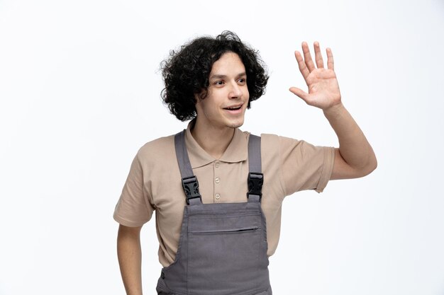 Impressed young male construction worker wearing uniform looking at side doing hi gesture isolated on white background