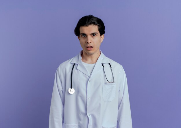 복사 공간 보라색 벽에 고립 된 의료 가운과 청진기를 입고 감동 된 젊은 남성 의사