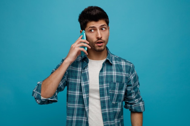 Free photo impressed young man talking on phone looking at side isolated on blue background