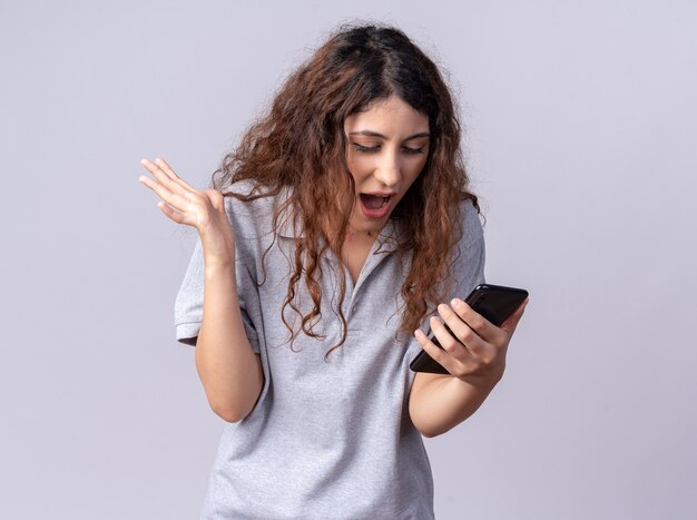 Free photo impressed young pretty caucasian girl holding and looking at mobile phone showing empty hand isolated on white wall with copy space