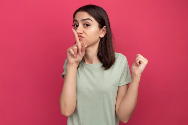 Impressed young pretty caucasian girl pointing behind doing keep silence gesture 