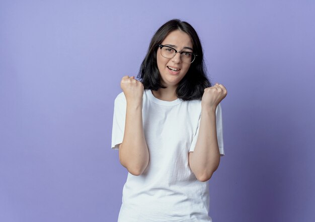Impressed young pretty caucasian girl wearing glasses clenching fists isolated on purple background with copy space