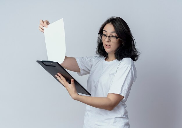 Impressed young pretty caucasian girl wearing glasses holding and looking at clipboard isolated on white background with copy space