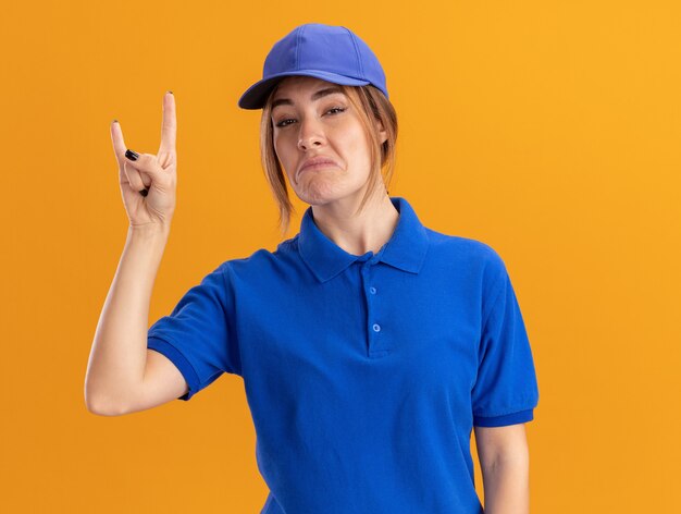 Impressed young pretty delivery woman in uniform gestures horns hand sign isolated