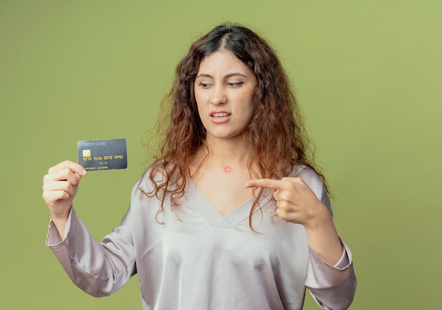 впечатлен молодой симпатичный женский офисный работник держит и указывает на кредитную карту