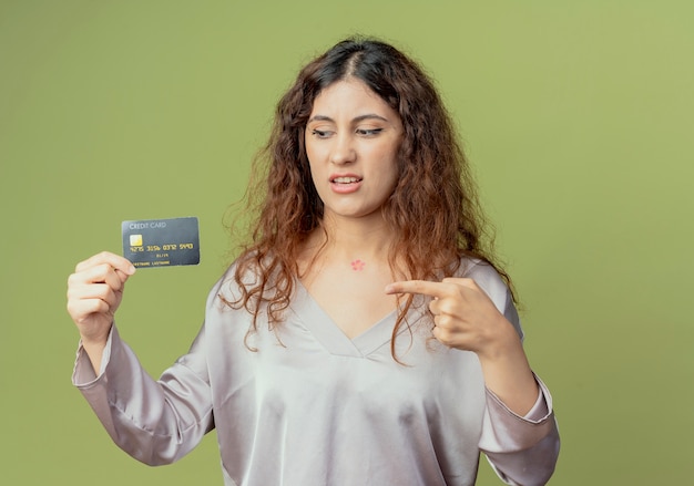 impressed young pretty female office worker holding and points at credit card