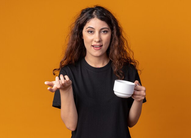 Impressed young pretty girl holding cup of tea looking and pointing at camera 