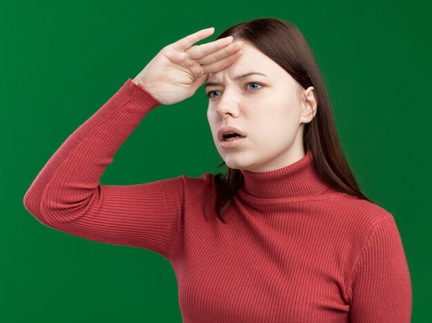 Impressed young pretty girl keeping hand on forehead looking at side into distance 