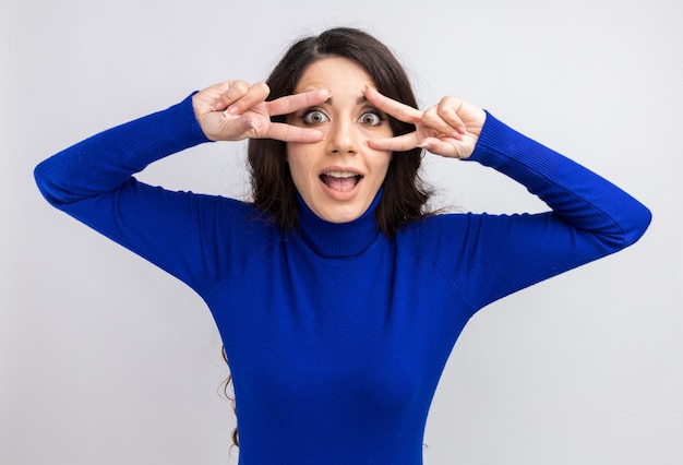 Free photo impressed young pretty girl showing v-sign symbols near eyes