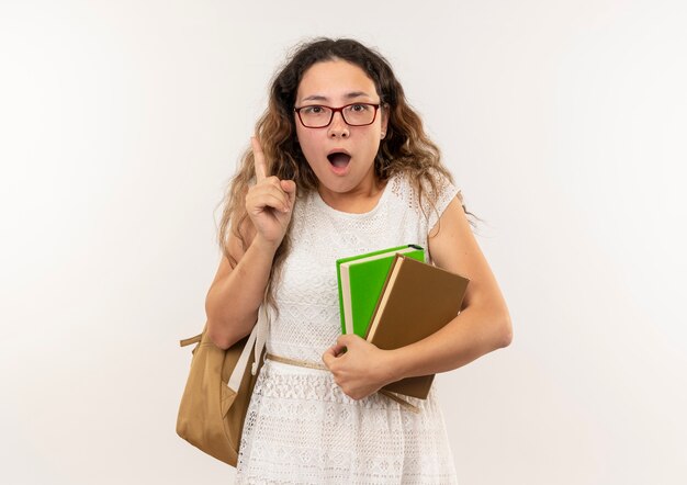 Impressed young pretty schoolgirl wearing glasses and back bag holding books raising finger isolated on white