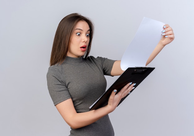 Impressed young pretty woman holding and looking at clipboard isolated on white background with copy space