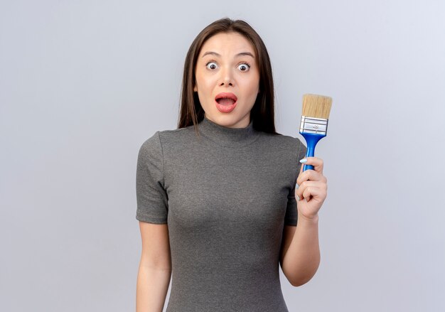 Impressed young pretty woman holding paint brush isolated on white background with copy space