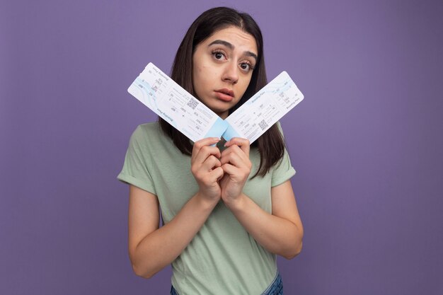 Impressed young pretty woman looking at front holding airplane tickets looking at front isolated on purple wall with copy space