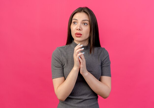 Impressionato giovane donna graziosa che mette le mani insieme guardando il lato isolato su sfondo rosa con spazio di copia