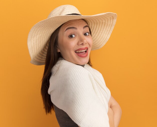 Impressed young pretty woman wearing beach hat standing in profile view  isolated on orange wall