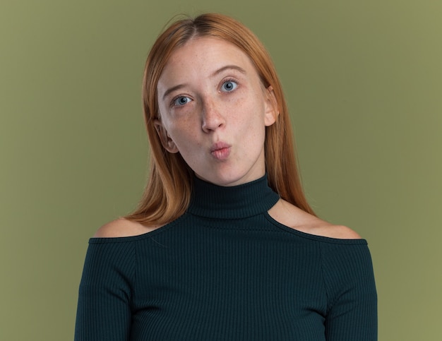 Impressed young redhead ginger girl with freckles isolated on olive green wall with copy space