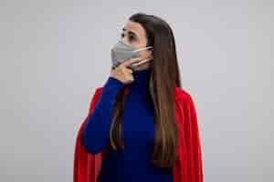 Free photo impressed young superhero girl looking at side wearing medical mask putting hand under chin isolated on white
