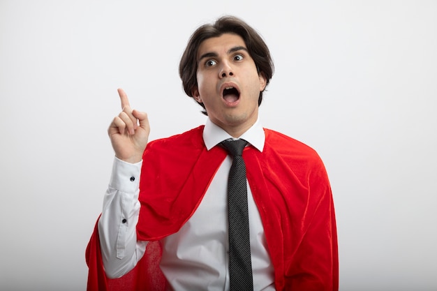 Impressed young superhero guy looking at side wearing tie points at side isolated on white background with copy space