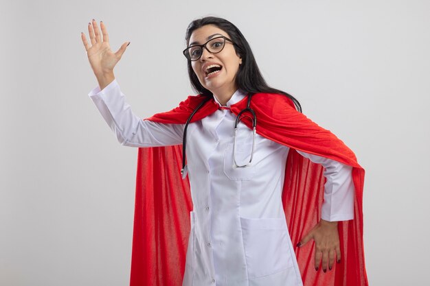 Impressed young superwoman wearing glasses and stethoscope looking at front doing robot dance isolated on white wall