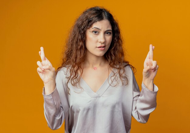 impressed young woman crossing fingers isolated on yellow