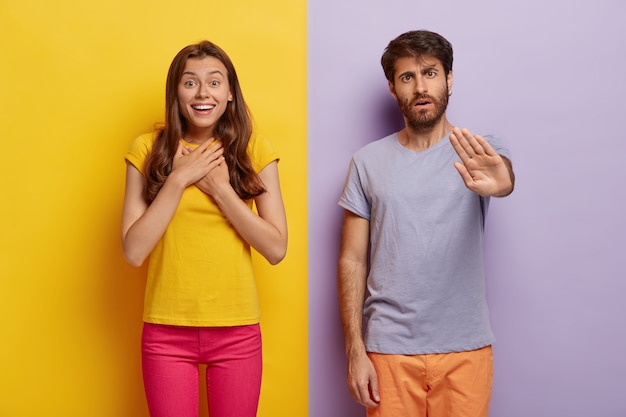 Foto gratuita la giovane donna colpita si sente eccitata e felice, tiene le mani sul petto, un uomo serio con la barba lunga fa un gesto di arresto, si avvicina l'uno all'altro