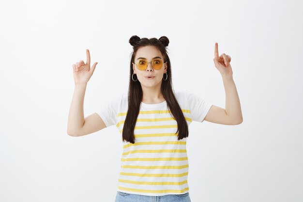 Impressed young woman posing with sunglasses against white wall