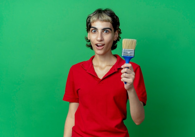 impressed young woman with pixie haircut holding paint brush