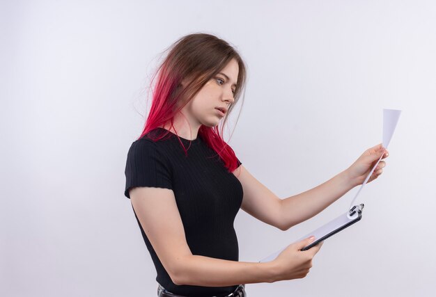 Impressive young beautiful woman wearing black t-shirt flipping throught clipboard in her hand on isolated white wall