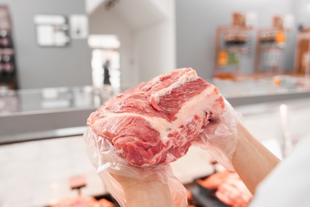 Free photo incognito female butcher showing meat behind counter.